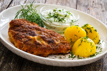 Breaded fried pork chop with fresh cucumber in cream and potatoes on wooden table 