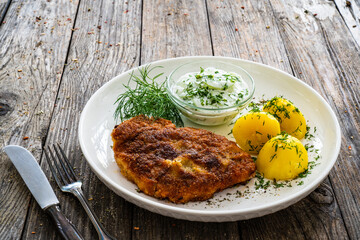 Breaded fried pork chop with fresh cucumber in cream and potatoes on wooden table 