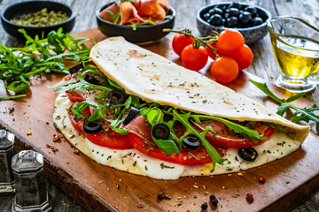 Italian piada wraps - piadina filled with fresh vegetable leaves, prosciutto crudo, mozzarella and tomatoes on wooden table
