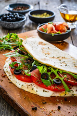 Italian piada wraps - piadina filled with fresh vegetable leaves, prosciutto crudo, mozzarella and tomatoes on wooden table
