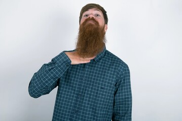 red haired man wearing plaid shirt over white studio background cutting throat with hand as knife,...