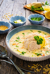 Greek lemon creamy soup with cooked chicken breast on wooden table


