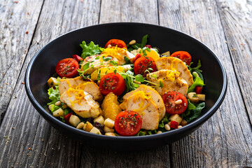 Tasty Greek salad - fried chicken breast, halloumi cheese, oranges, pine nuts, raisins, mini tomatoes and fresh green vegetables on wooden background
