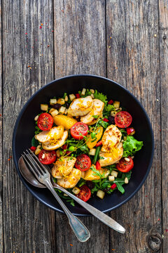 Tasty Greek salad - fried chicken breast, halloumi cheese, oranges, pine nuts, raisins, mini tomatoes and fresh green vegetables on wooden background
