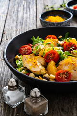 Tasty Greek salad - fried chicken breast, halloumi cheese, oranges, pine nuts, raisins, mini tomatoes and fresh green vegetables on wooden background
