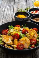 Tasty Greek salad - fried chicken breast, halloumi cheese, oranges, pine nuts, raisins, mini tomatoes and fresh green vegetables on wooden background
