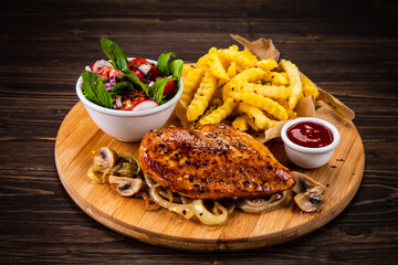 Roast chicken breast, French fries, fried mushrooms and fresh vegetables on wooden table
