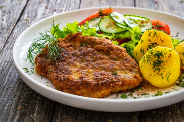 Breaded fried pork chop with fresh vegetable salad and potatoes on wooden table
