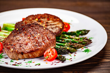Barbecued beef steak with green asparagus on wooden table
