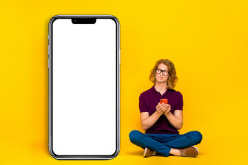 Full size photo of strict ginger guy sit hold telephone look promo wear eyewear casual cloth isolated on yellow background
