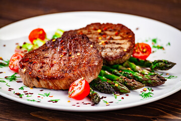 Barbecued beef steak with green asparagus on wooden table

