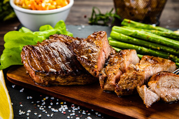 Barbecued pork french fries asparagus and vegetables on black stone plate
