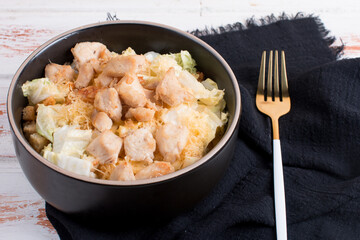 vegetable salad with fried chicken breast in a deep dish. Serving on a wooden background with a black napkin and cutlery