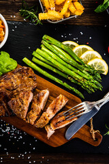 Barbecued pork french fries asparagus and vegetables on black stone plate
