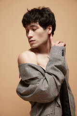 Portrait of young asian man posing shirtless in stylish checkered grey jacket against light brown studio background. Concept of male body aesthetics, style, health, men's beauty and fashion