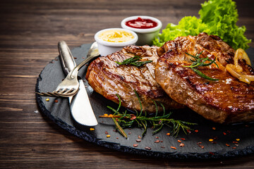 Fried beef sirloin with lettuce, ketchup and mustard on black stone plate on wooden table

