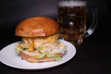 Delicious classic burger with cutlet and glass of cold beer on a black background. Harmful and fast food.