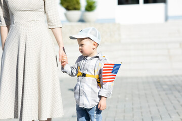 A boy with his mother stands near the administrative building and holds the flag of America in his...