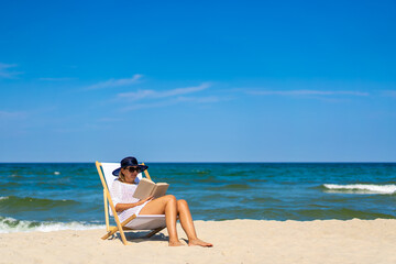 Woman relaxing on beach reading book sitting on sunbed
