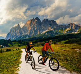 Naklejka na ściany i meble A man and woman ride electric mountain bikes in the Dolomites in Italy. Mountain biking adventure on beautiful mountain trails.