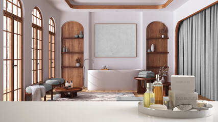 Spa, hotel bathroom concept. White table top or shelf with bathing accessories, toiletries, over minimalist bathroom in japandi apartment, freestanding bathtub, modern interior design