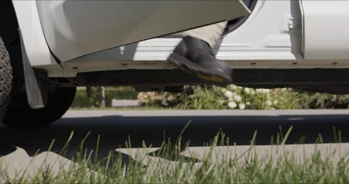 Closeup shot of a man in work boots getting out of the white truck on a sunny day