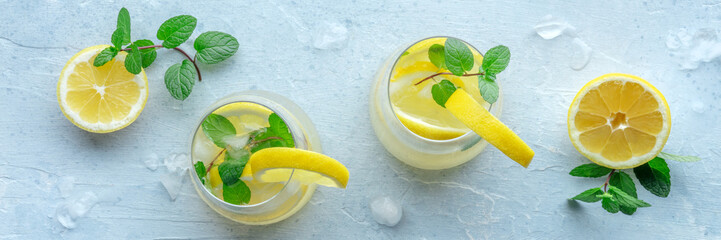 Lemonade with mint panorama. Lemon water drink with ice. Two glasses and lemons on a pastel...