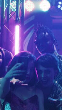 Vertical video: Diverse people taking photos at club, recording video and having fun at dance party with electronic music. Funky smiling men and women enjoying discolights and taking pictures.