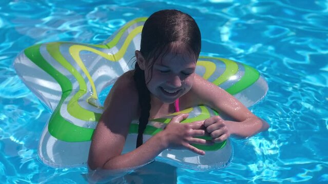 Smiling cute little girl with swim ring in swimming pool on sunny day. Childhood summer vacation concept. Happy kid playing. Healthy outdoor sport activity for children. Kids beach fun