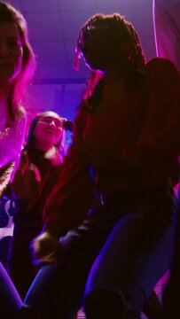Vertical video: POV of friends dancing at disco party, enjoying social gathering with modern clubbing music on dance floor. Group of people having fun together at dance event in discotheque. Handheld