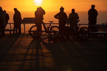 Fototapeta na wymiar Silhouettes of people with bicycles in sunset contour light, evening orange sun