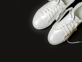 White leather shoes on a black background. White sneakers with white laces. New shoes. Horizontal image.