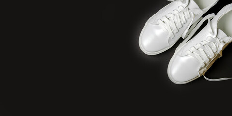 White leather shoes on a black background. White sneakers with white laces. New shoes. Horizontal image. Banner for insertion into site.