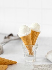 Cones of vanilla icecream in a glass, served in a bright kitchen, with cones and ice-cream scooper