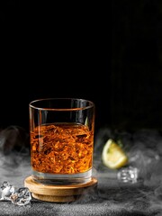 Vertical shot of a glass of alcohol with ice next to it surrounded by smoke on black background