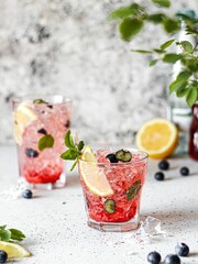 Vertical shot two fresh summer iced drinks garnished with lemon, and blueberries, a vertical shot