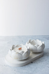 Handmade candles from paraffin and soy wax in plaster candlestick on white concrete podium on pastel gray background. Copy space