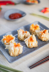 Steamed chicken dimsum served on plate with chili, tomato and sauce as background on wooden table