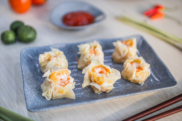 steamed prawn dimsum served on plate with chili, tomato and sauce as background on wooden table