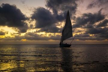 Fototapeta na wymiar Sailboat in the calm waters of the sea with the sunset in the cloudy background