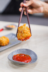 close up hand with fried dim sum, dipping fried dim sum in bowl of tomato sauce on wooden table