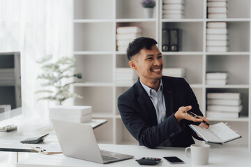 Fototapeta premium Happy working asian businessman talking on the phone with accounting documents at desk in happy working office
