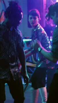 Vertical video: Young people partying at nightclub, having fun dancing on electronic music. Cheerful persons enjoying party and showing dance moves at discotheque, live performance. Handheld shot.