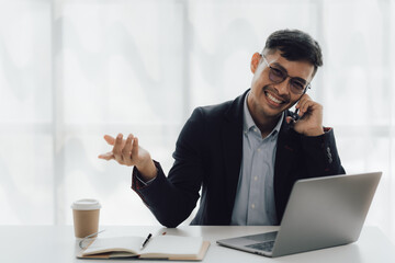 Happy working asian businessman talking on the phone with accounting documents at desk in happy working office