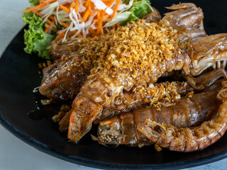 Deep fried crayfish with topping garlic on the black dish served with vegetables on the table, Asian delicious seafood. Stir fried crayfish or mantis shrimps with garlic and pepper cuisine.