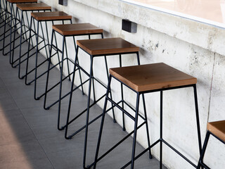 Row of wooden bar stool chairs beside concrete counter bar, loft style cafe interior. Empty wood...