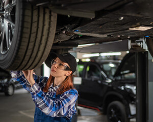 Fototapeta na wymiar A female mechanic inspects a lifted car. A girl at a man's work.