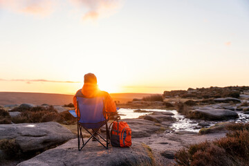 Bearded  Man in orange jacket relaxing alone on the top of  mountain  and drinking hot coffee at sunrise. Travel  Lifestyle concept The national park Peak District in England