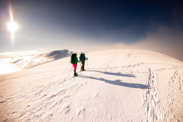 two girls with a backpack and snowshoes walk in the snow during a snow storm.