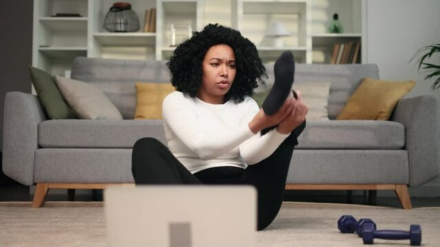 Funny african american young woman with puzzled face looks at hard fitness sport workout of online trainer unsuccessfully tries to repeat and looking at camera shrugs at home alone Beginner concept 